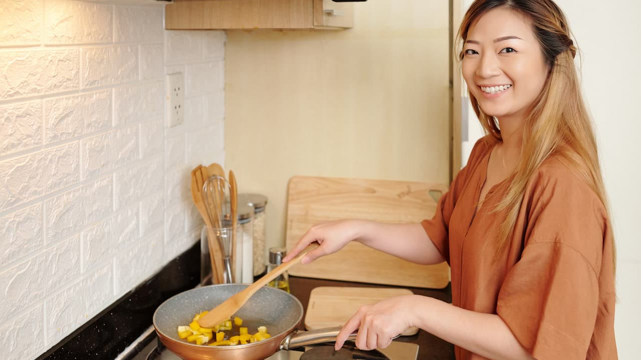 Alicia souriante dans sa cuisine, spatule en bois à la main au-dessus d'une poêle