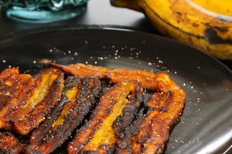 Delicieuses tranches de plantain frit servies sur une assiette noire, idéales pour la photographie culinaire