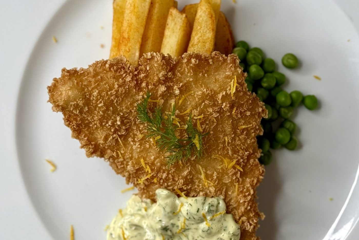Crispy fish and chips served with peas and tartar sauce on a white plate. Poisson et frites croustillants servis avec des petits pois et une sauce tartare sur une assiette blanche.