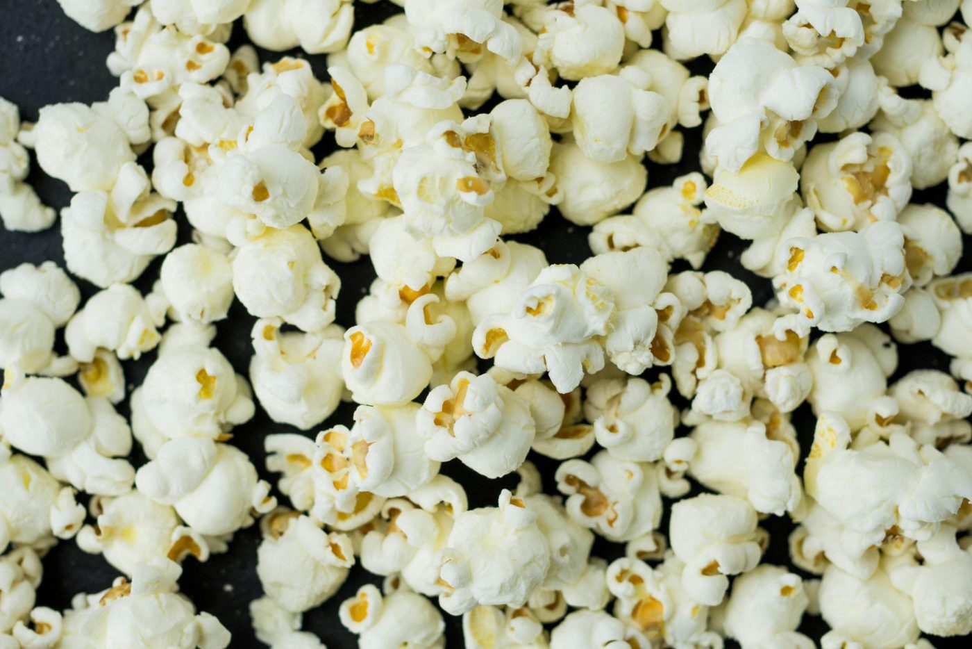 A close-up view of freshly popped popcorn scattered on a dark surface, ideal as a snack. Une vue rapprochée de pop-corn fraîchement éclaté éparpillé sur une surface sombre, idéal comme collation.