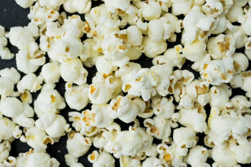 A close-up view of freshly popped popcorn scattered on a dark surface, ideal as a snack. Une vue rapprochée de pop-corn fraîchement éclaté éparpillé sur une surface sombre, idéal comme collation.