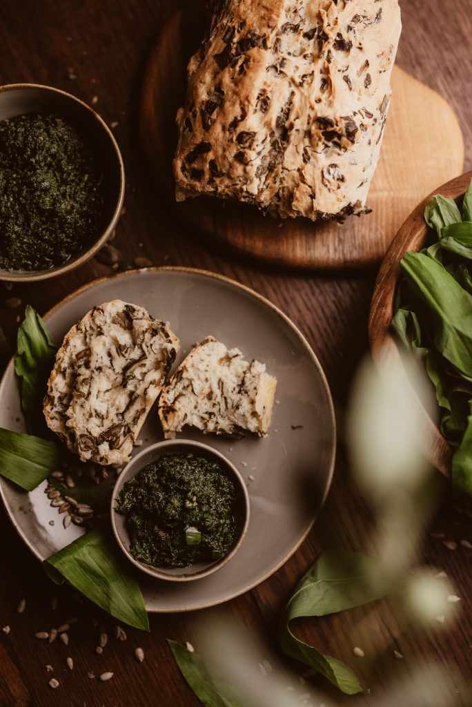 Fresh herb pesto served with rustic wholemeal bread on a wooden table. Pesto aux herbes fraîches servi avec du pain complet rustique sur une table en bois.