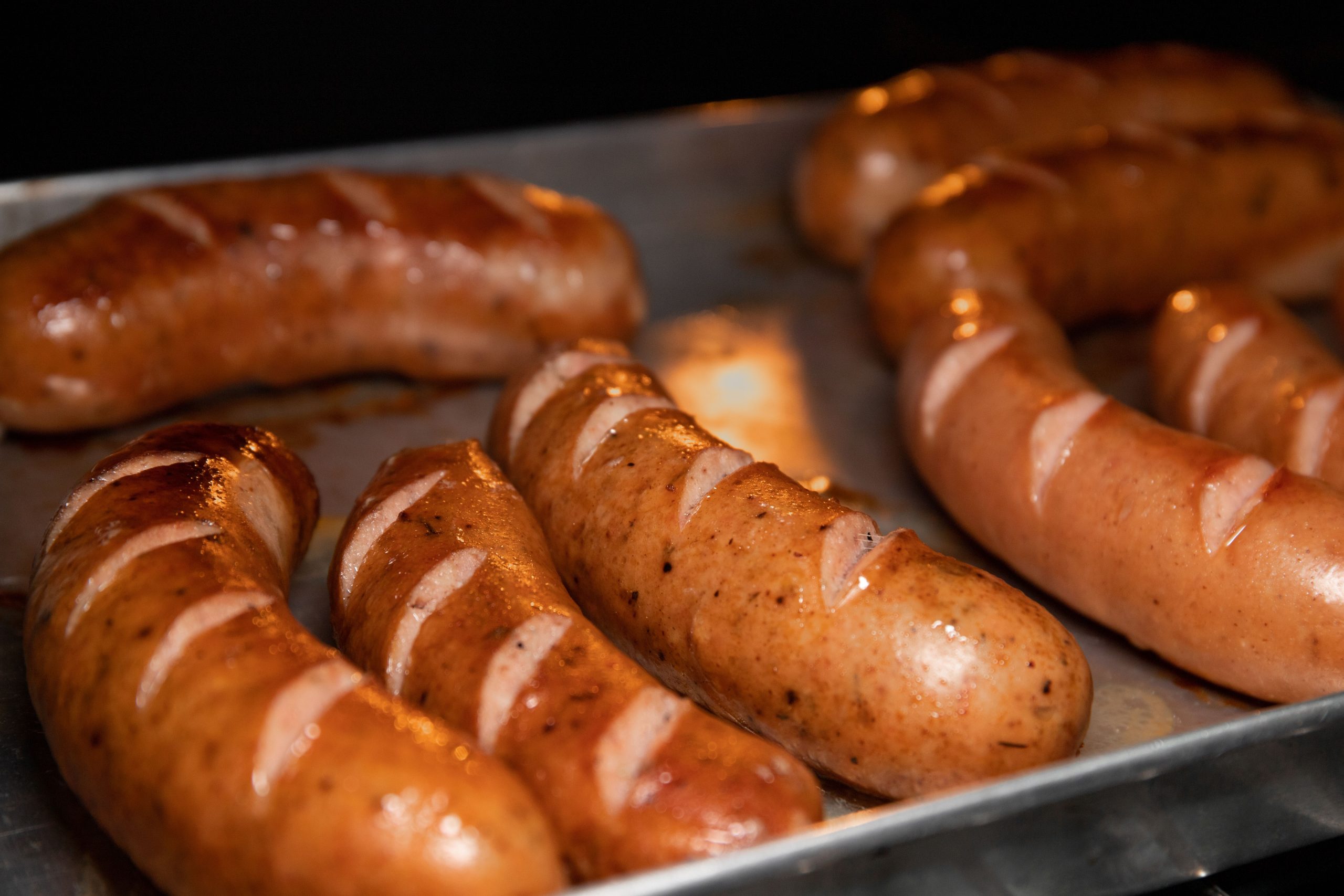 A close-up of juicy grilled sausages on a metal tray, perfect for food lovers. Gros plan de saucisses grillées juteuses sur un plateau métallique, parfait pour les amateurs de nourriture.