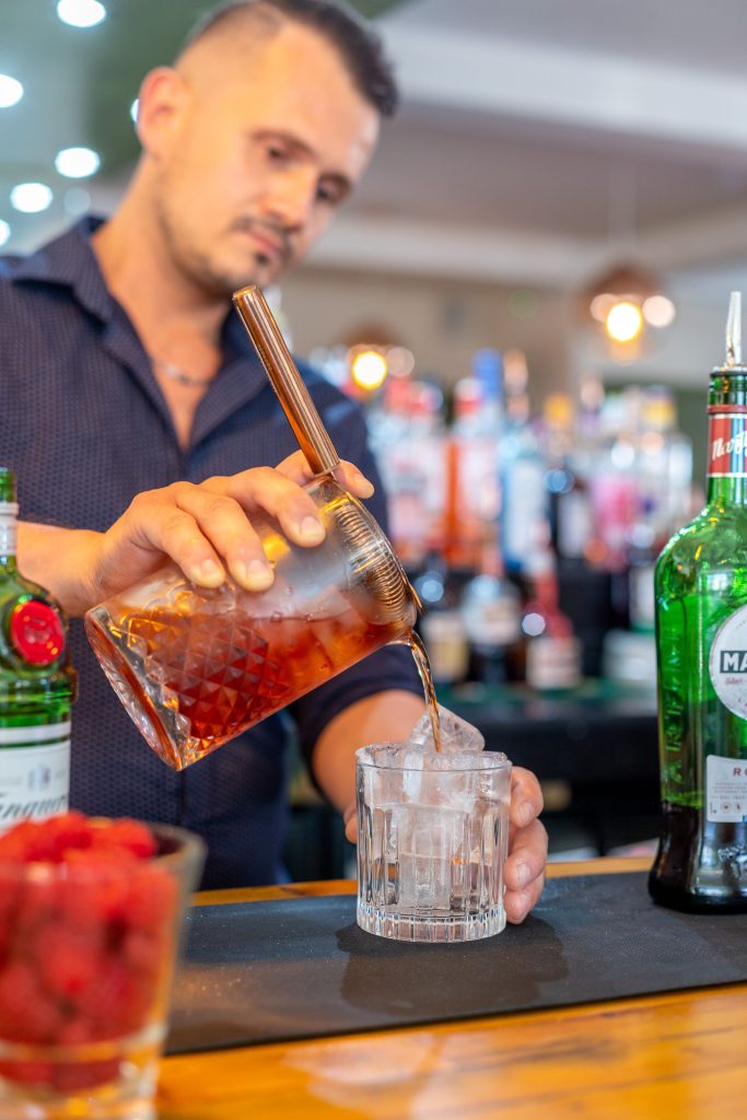 Bartender at a London bar pouring a cocktail over ice in a vibrant setup. Barman dans un bar de Londres versant un cocktail sur de la glace dans un cadre vibrant.