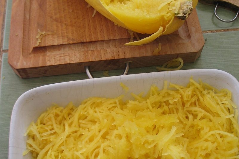 Moitié de courge spaghetti cuite sur une planche, filaments jaunes détachés à la fourchette et plat de filaments