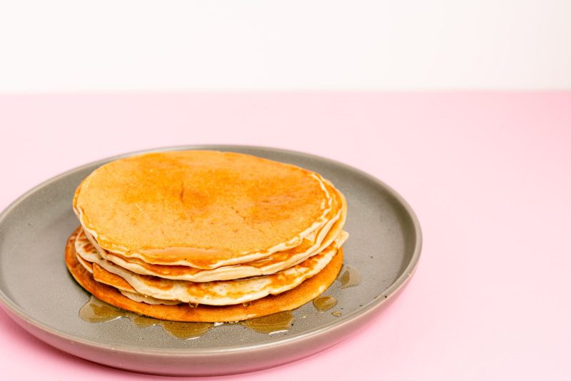 Pile de pancakes nappés de sirop sur fond rose