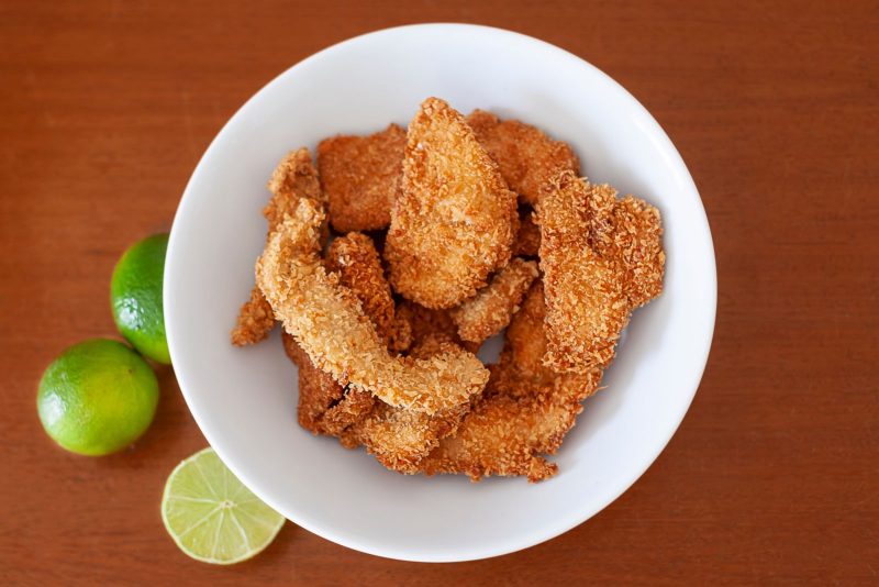 Lanières de poisson pané dans une assiette, citrons verts à côté