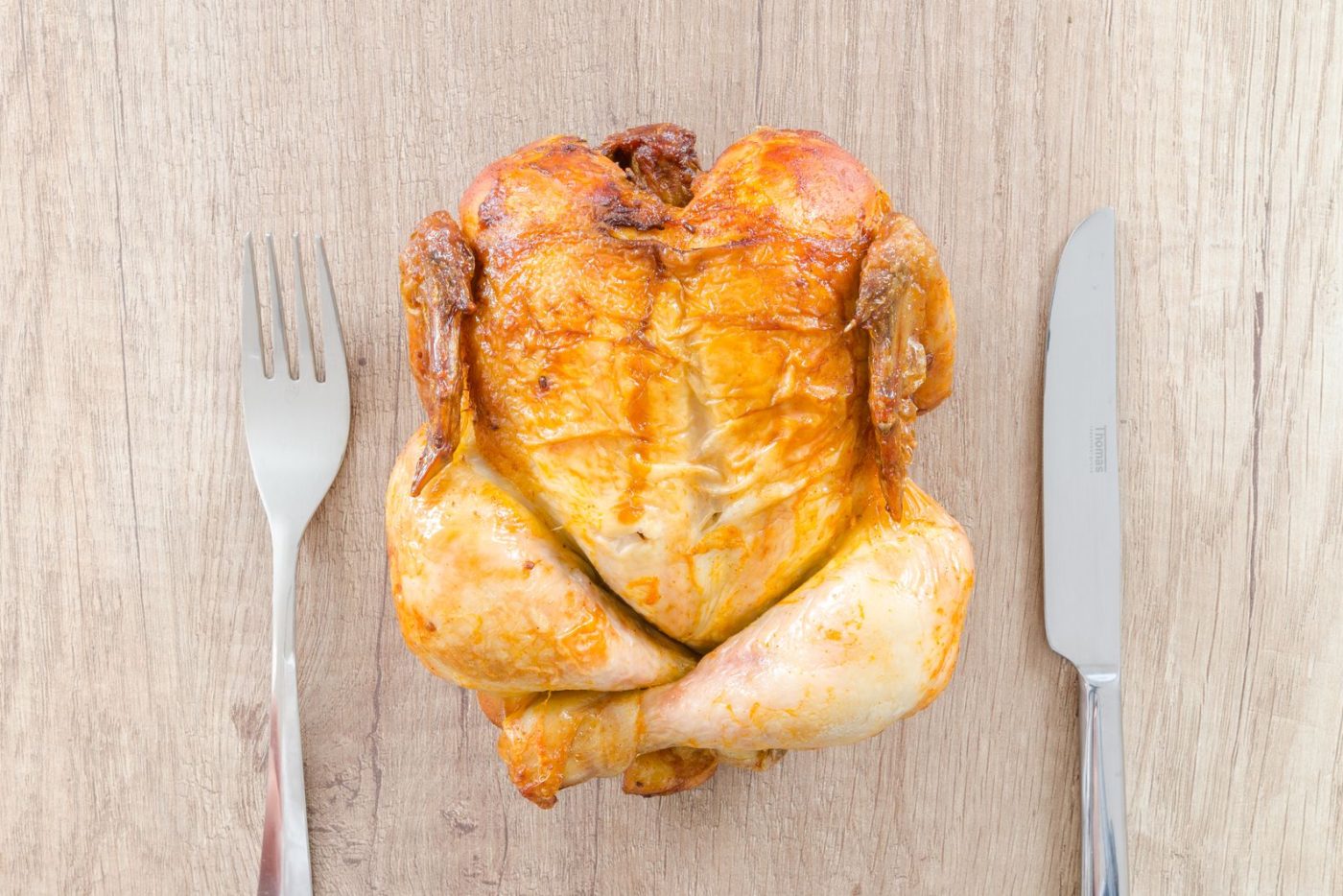 Poulet rôti entier entre un couteau et une fourchette