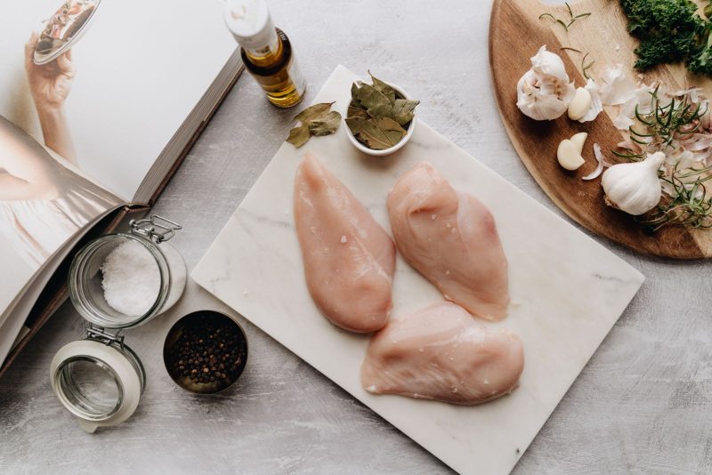Filets de poulet crus sur une planche, avec ail, huile et bocaux d'épices, vue de dessus