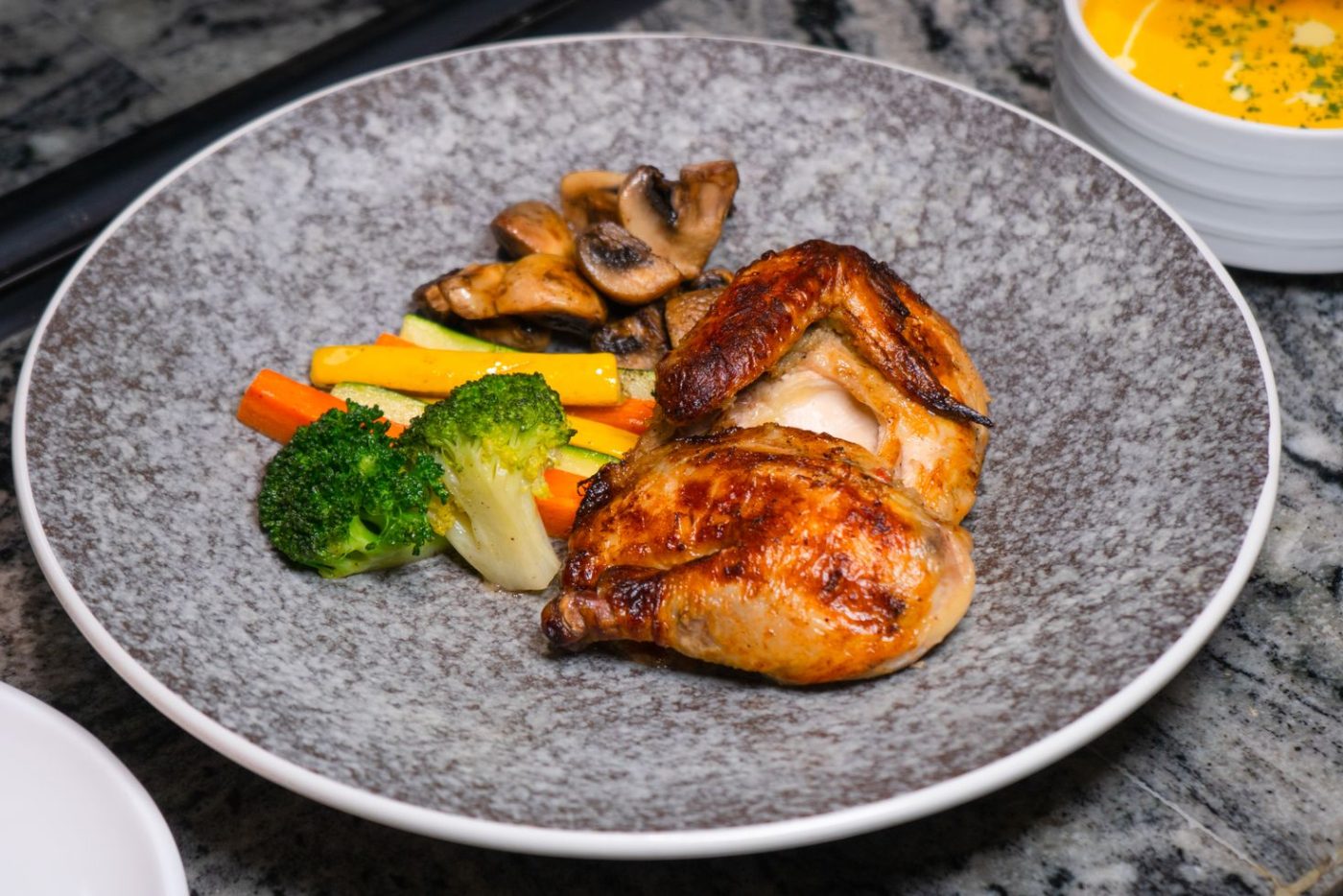Assiette grise garnie de poulet doré, de brocolis, de carottes et de champignons